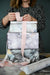 artful gift wrap on a stack of three boxes, Artist Dana Mooney stands behind the stack tying a pink ribbon bow on top.