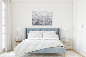 A calming grey painting hangs above a tufted light blue upholstered bed in an airy, white modern traditional bedroom. 