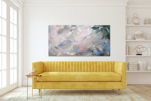 Above a yellow tufted modern sofa, a painting hangs horizontally on the wall.  Comprised of greens, pink and whites, it is modern and minimal, with expressive brushstrokes and colours. 